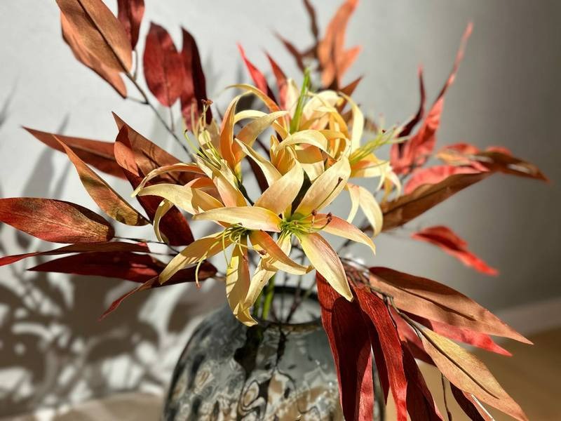Herbstliche Blätter, gelbe Blütenstrahlen, Keramikvase.