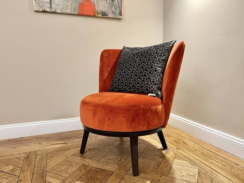 Orangener Sessel, gemusteres Kissen, Parkett.